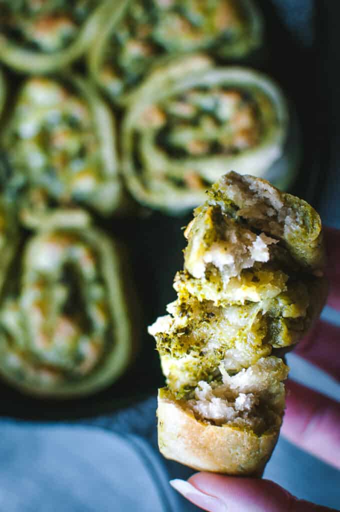 a close up shot of a hand holding a pesto pizza pinwheel