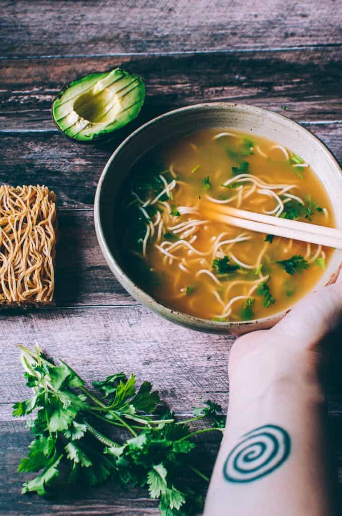 a bowl of ramen pho with avocado and cilantro by side