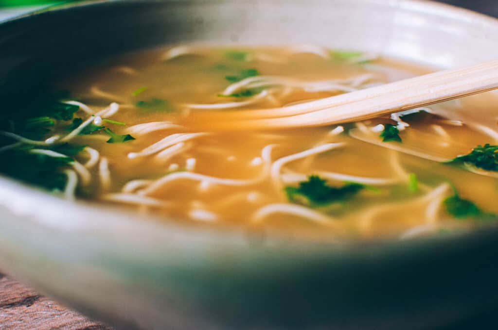a close up shot of noodles in an orange broth