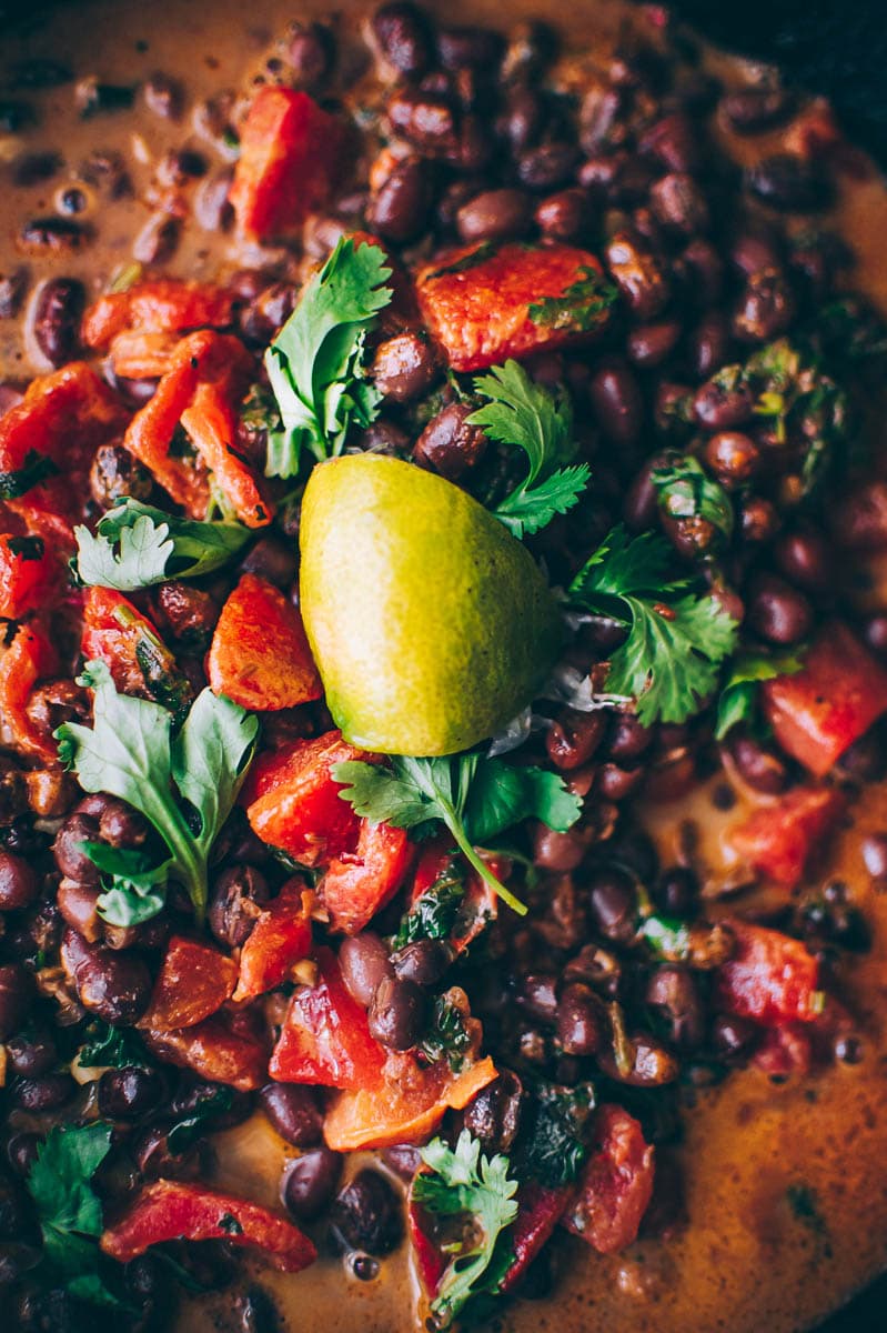 A close-up of black beans, diced tomatoes, and fresh cilantro topped with a lime wedge in a sauce inspired by Adzuki Bean Curry.