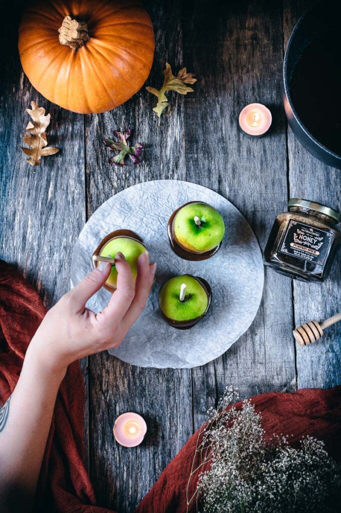 a hand reaching for a caramel apple amidst a wooden backdrop