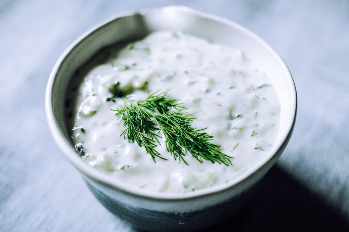 A ceramic bowl filled with white creamy sauce topped with fresh dill.