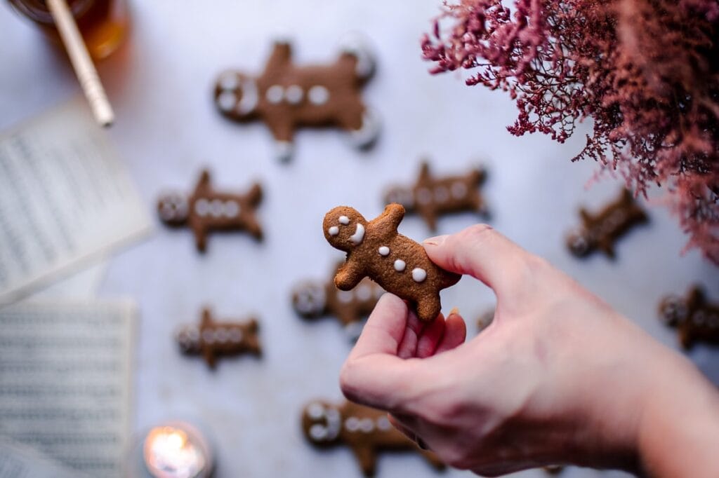 a hand holding a gingerbread man above a blurry background with music sheet book pages