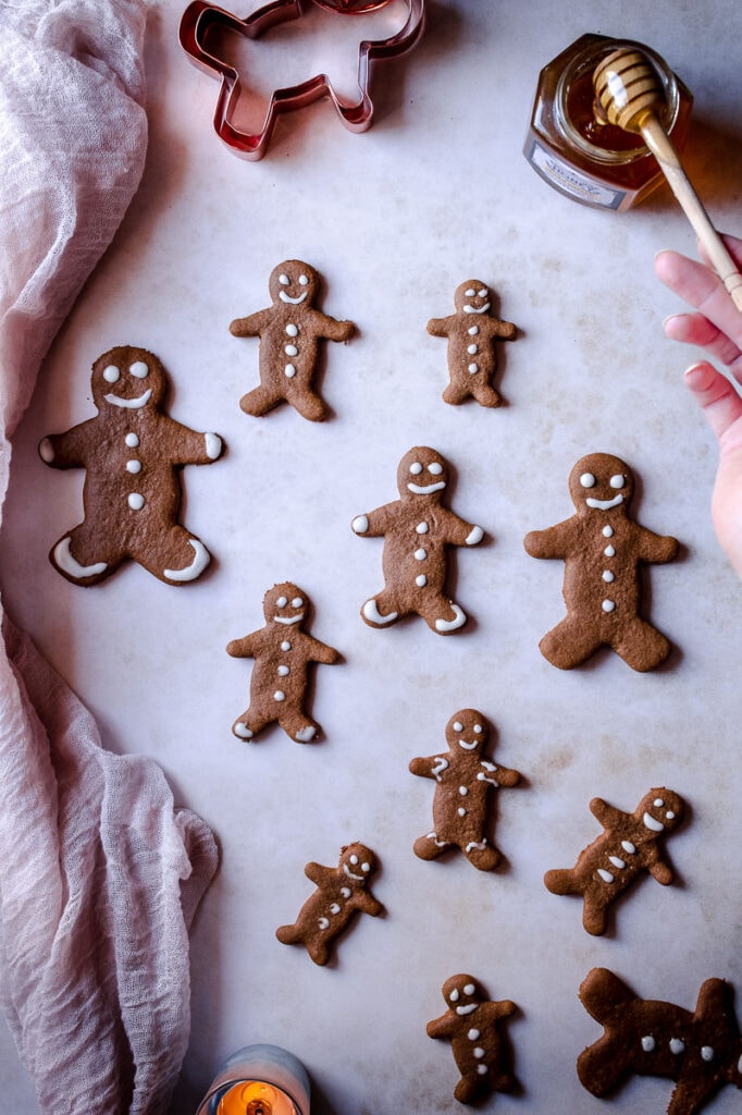 a hand holding a honey spoon on the edge of a collection of gluten-free gingerbread men 