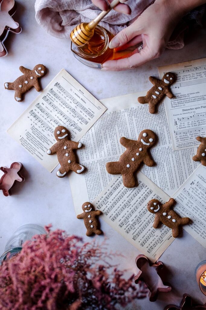 a hand holding a honey spoon dripping with honey next to music sheets and gluten free gingerbread men cookies