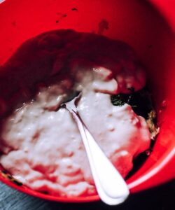 a red bowl of tzatziki being mixed with a spoon