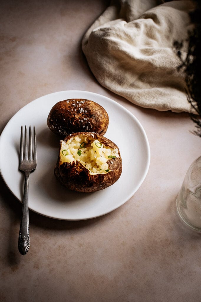flatlay style photo of baked potatoes fork cloth and plant