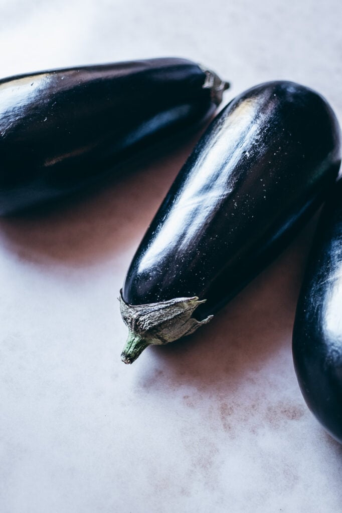 Three black eggplants on a white surface, ready for cooking in an air fryer.