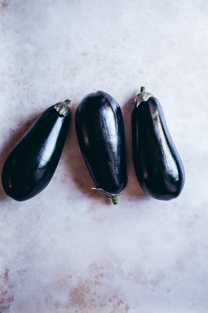 Three black eggplants on a white surface, perfect for preparing in an air fryer.