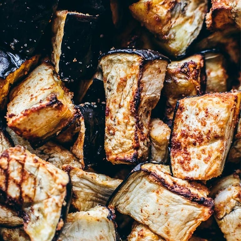 Close-up of air fryer eggplant cubes with a golden brown, slightly charred surface, seasoned with spices.