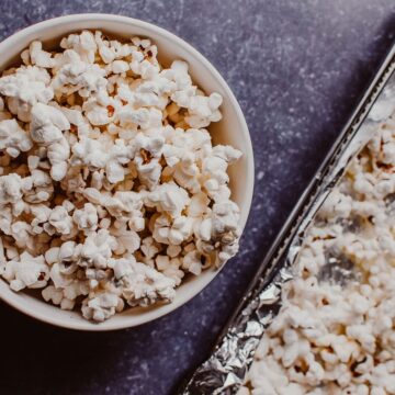 a white bowl filled with popcorn next to an air fryer tray filled with popcorn