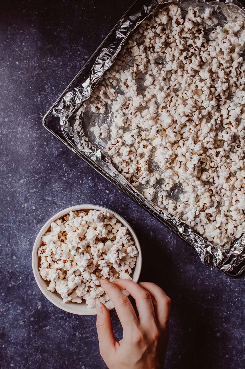 A hand grabbing air fryer popcorn from a white bowl on a blue countertop.