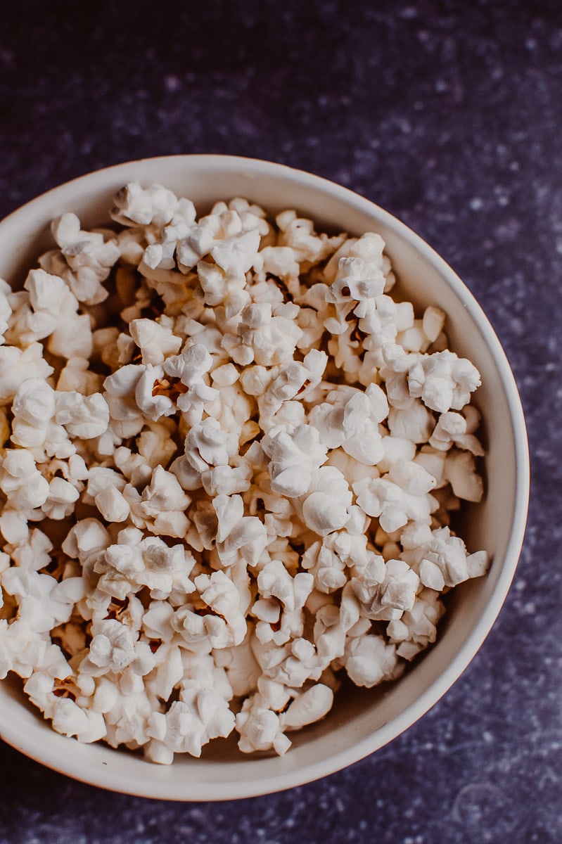 A close up shot of white fluffy popcorn in a white ceramic bowl.