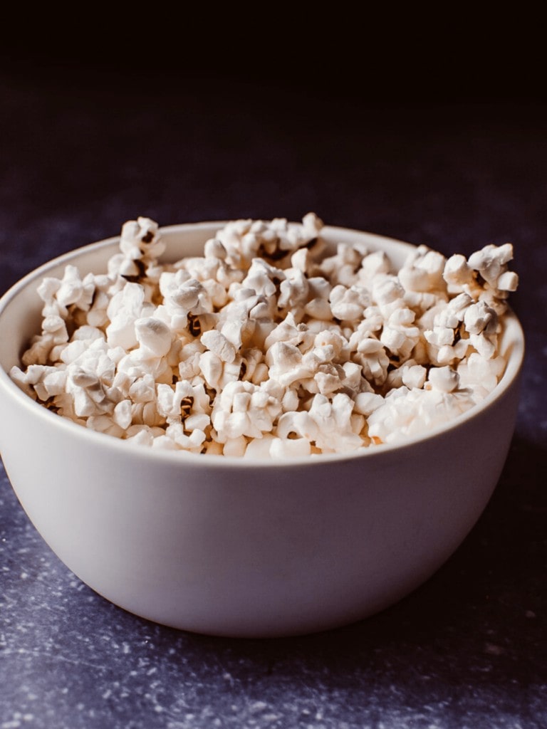 Air Fryer Popcorn in a white bowl on a dark blue backdrop