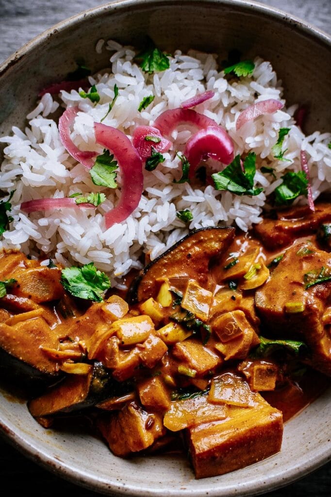 white rice topped with fresh cilantro and pickled red onion served next to curry with eggplant