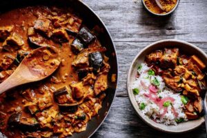 a pot of aubergine curry garnished with cilantro and pickled onion