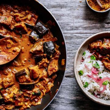 a pot of aubergine curry garnished with cilantro and pickled onion