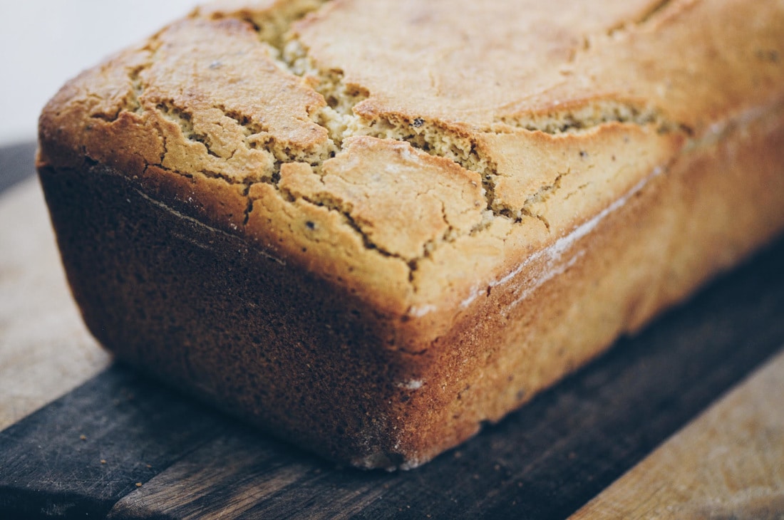 A close-up of a golden-brown loaf of bread resting on a wooden cutting board.