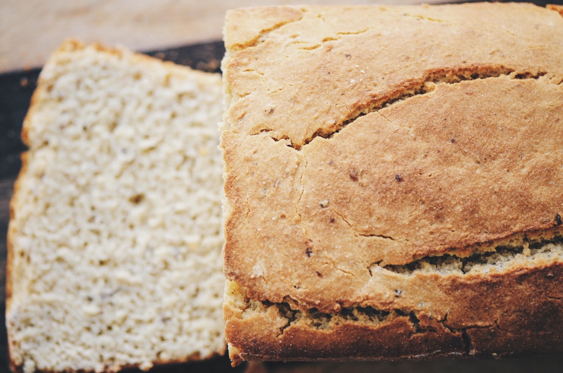 A close-up of a loaf of bread with one slice cut, showing the texture of the crust and the inside crumb.