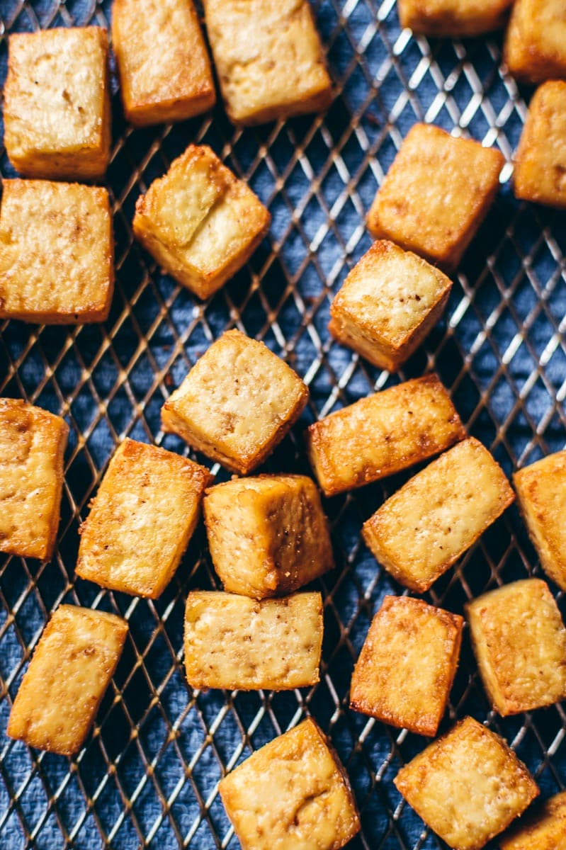 An air fryer basket try with crispy air fryer tofu scattered on top.