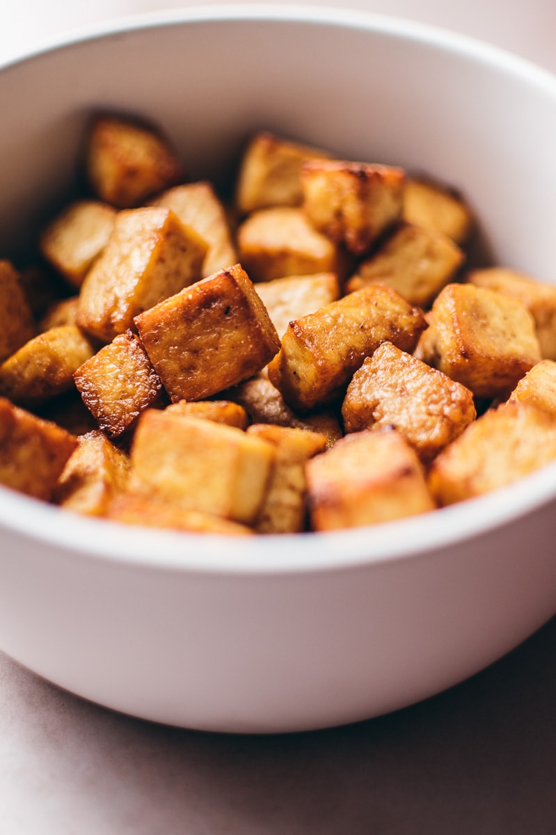 A close up shot of golden, crispy tofu in a white bowl.