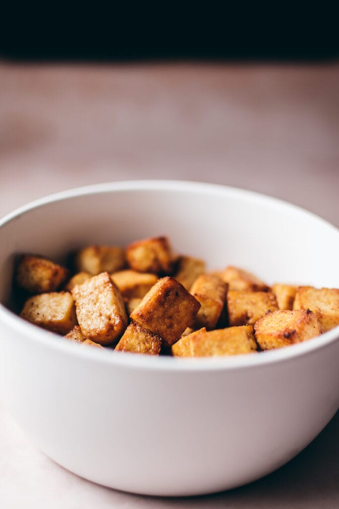 A white bowl of golden looking tofu.