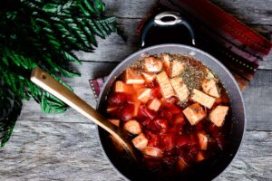 A pot of vegetarian stew with chopped vegetables and herbs, with a wooden spoon inside.