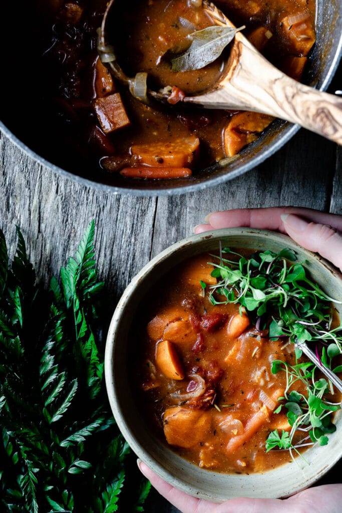 a hand holding a bowl of thick red stew