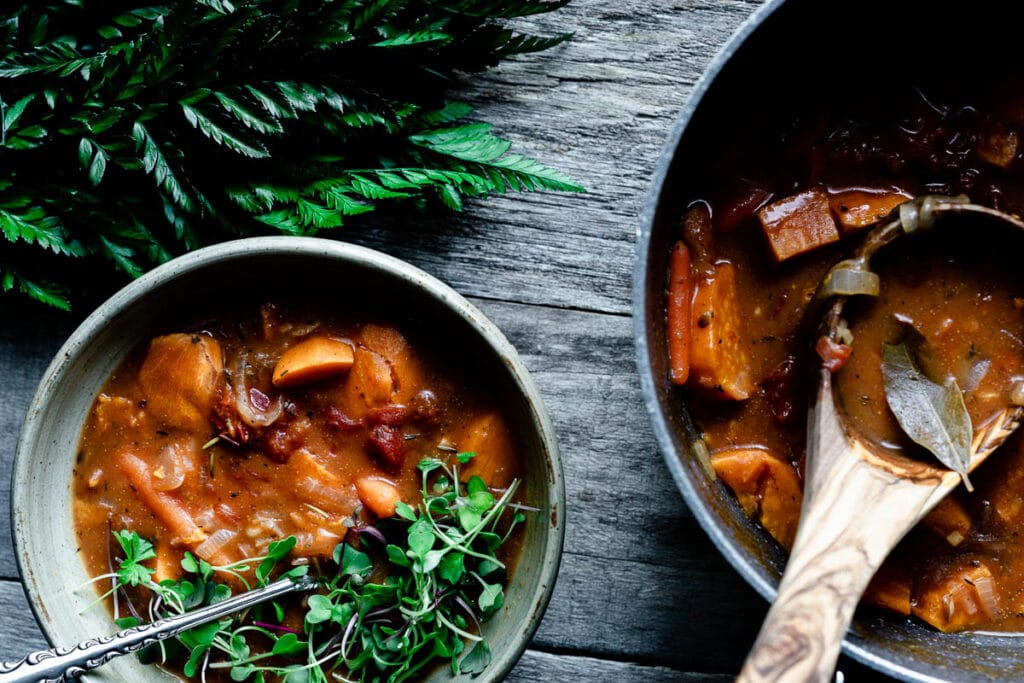 a bowl and a pot of stew with a wooden ladle