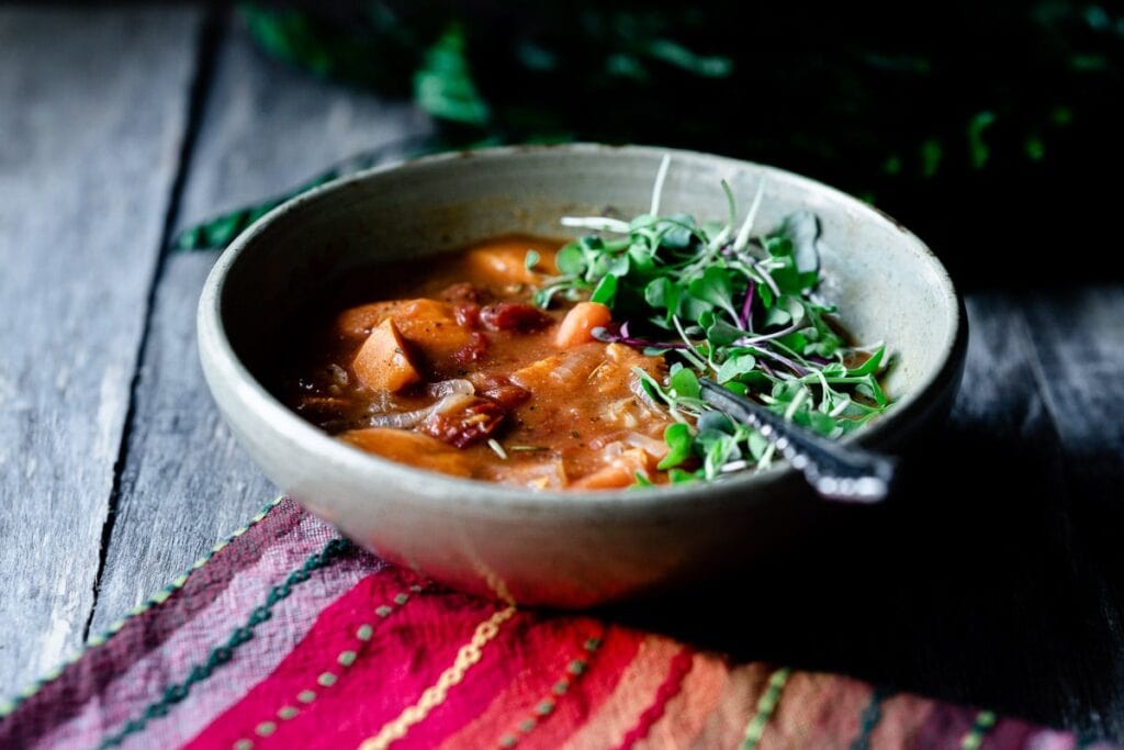 a side shot of a bowl of stew topped with green sprouts