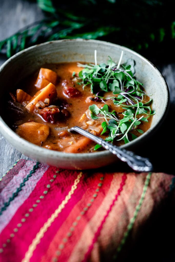 a spoon in a bowl of vegan stew topped with sprouts