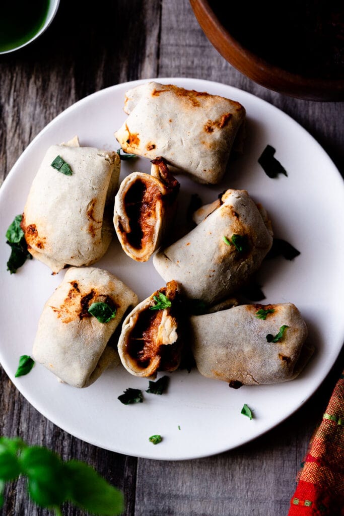 A white plate of air fried pizza rolls filled with red sauce and sprinkled with fresh basil.