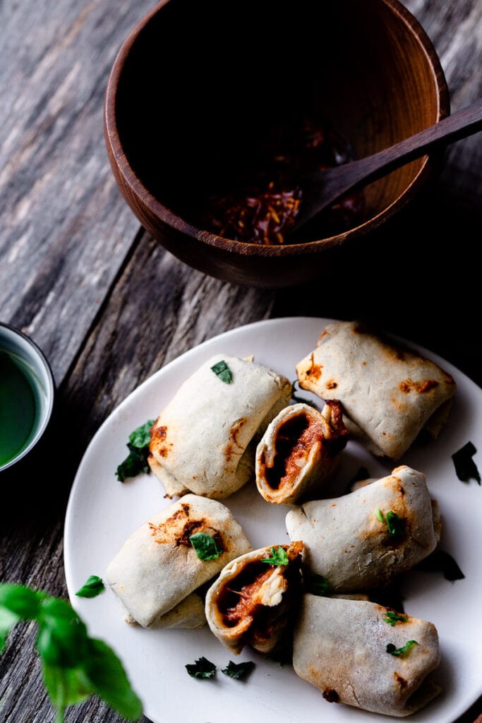 White pizza rolls resting on a white plate with fresh basil leaves.