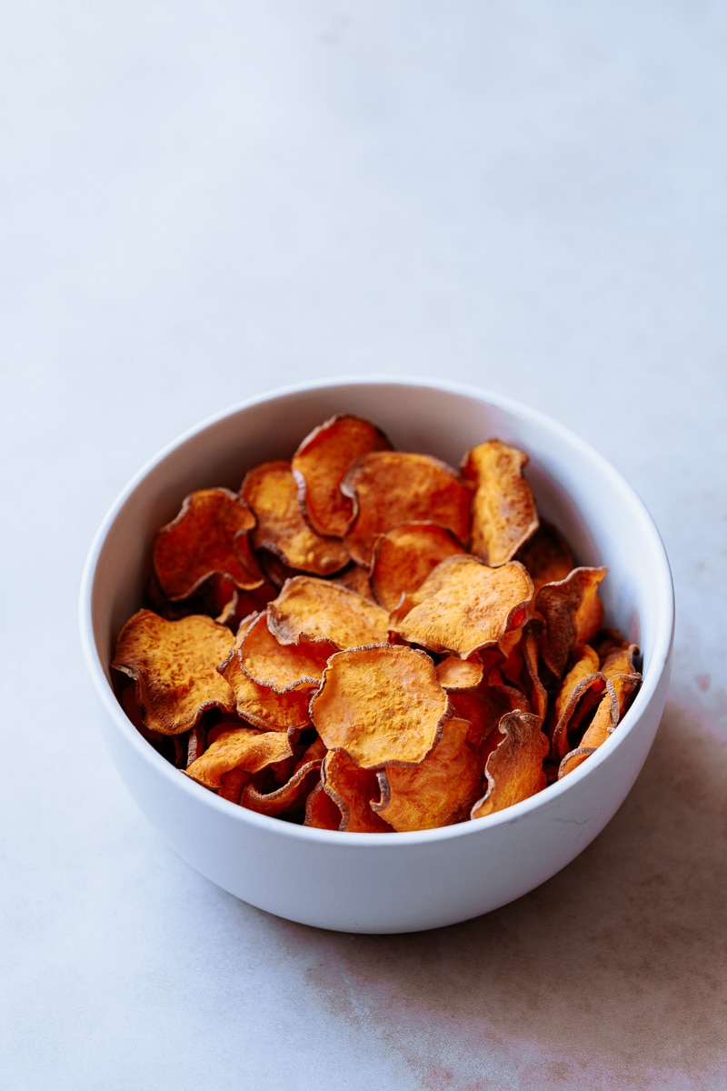 A white bowl filled with orange sweet potato chips.