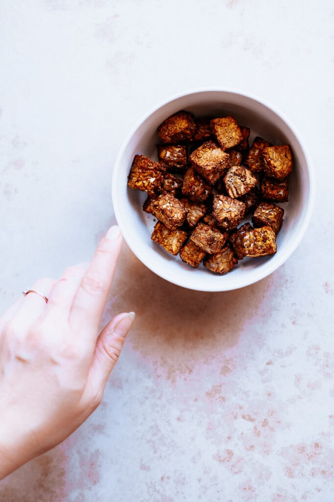 a hand reaching for a bowl of air fryer tempeh