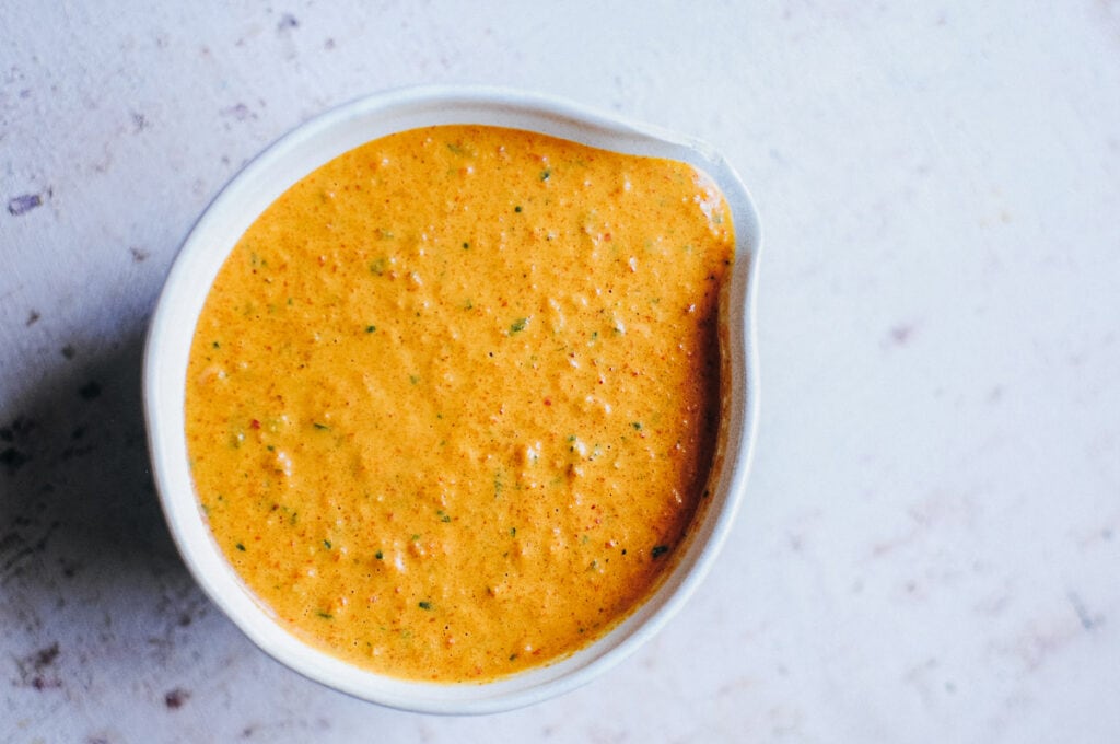 a top view of a ceramic dish filled orange red spanish romesco sauce