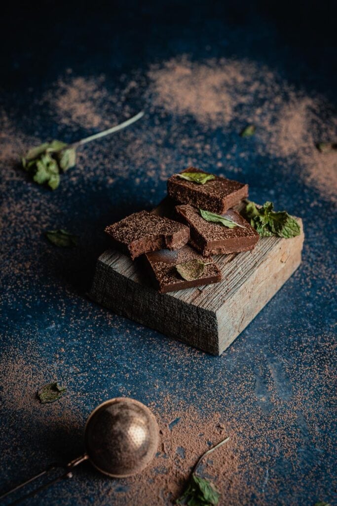 a stack of mint chocolate fudge on a wooden block dusted with fresh mint leaves and cacao powder