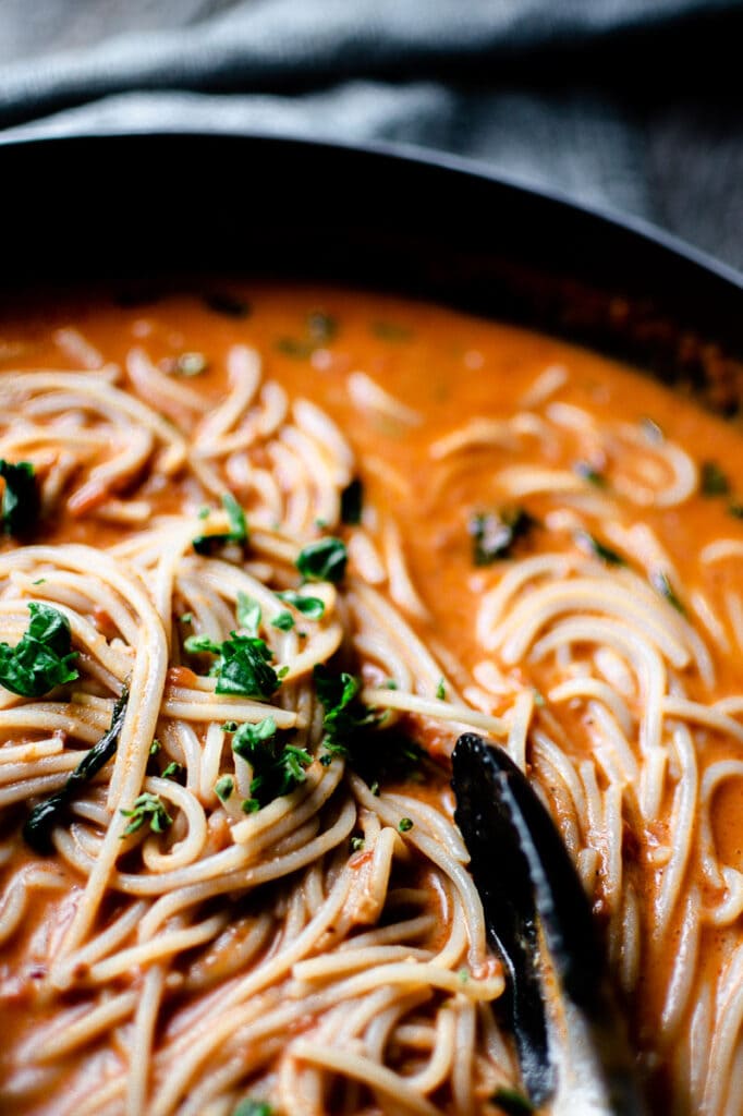 a creamy red pasta sauce in a pot of spaghetti noodles topped with basil