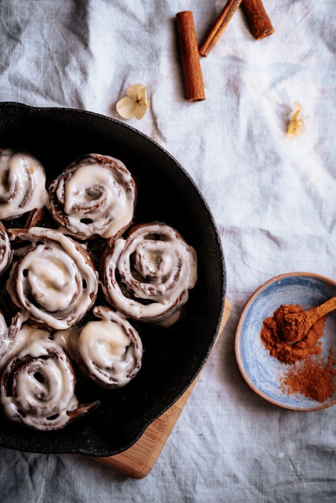 a cast iron pan filled with gluten free vegan cinnamon rolls drizzled with white icing