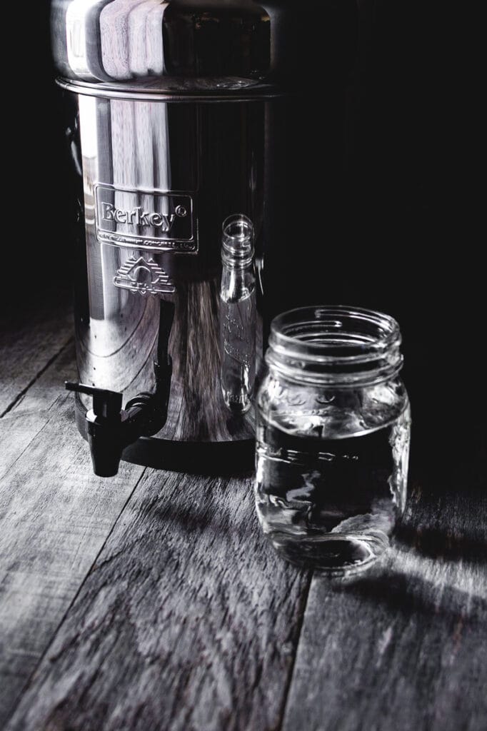 stainless steel berkey water filter system resting on wooden table next to backlit glass of water