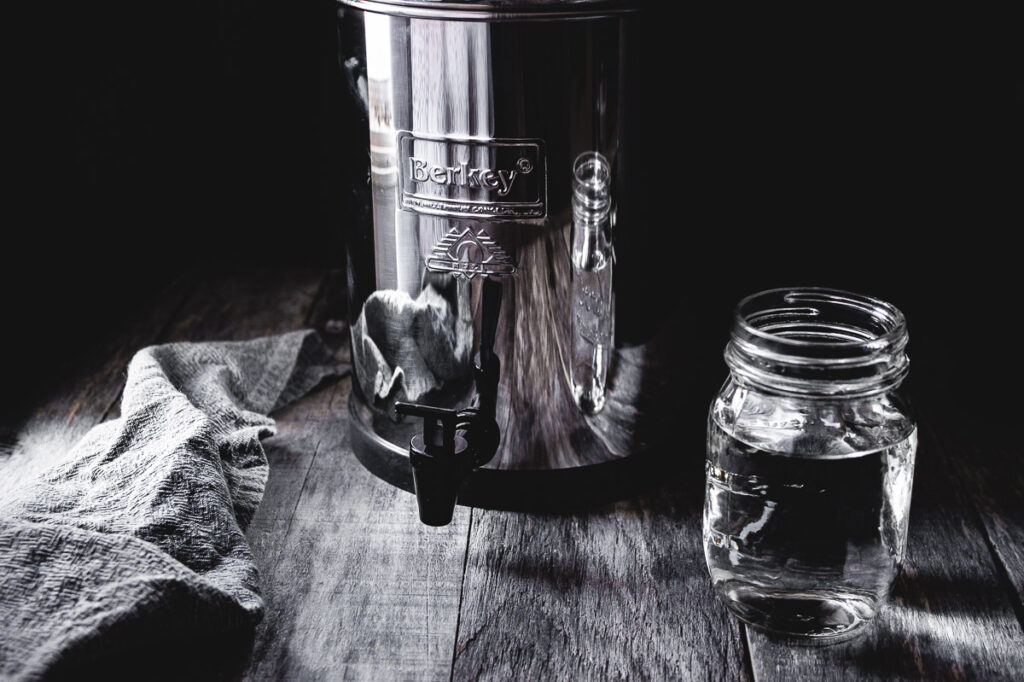 travel berkey water filter system on wooden table with a glass of water backlit