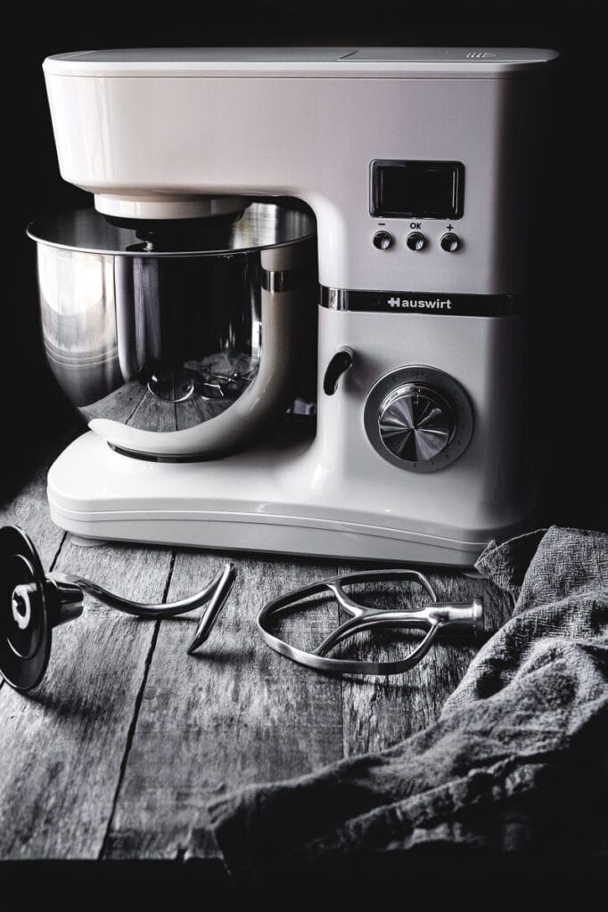 a shot of a hauswirt stand mixer and all of its attachments on a dark wooden table for a product review