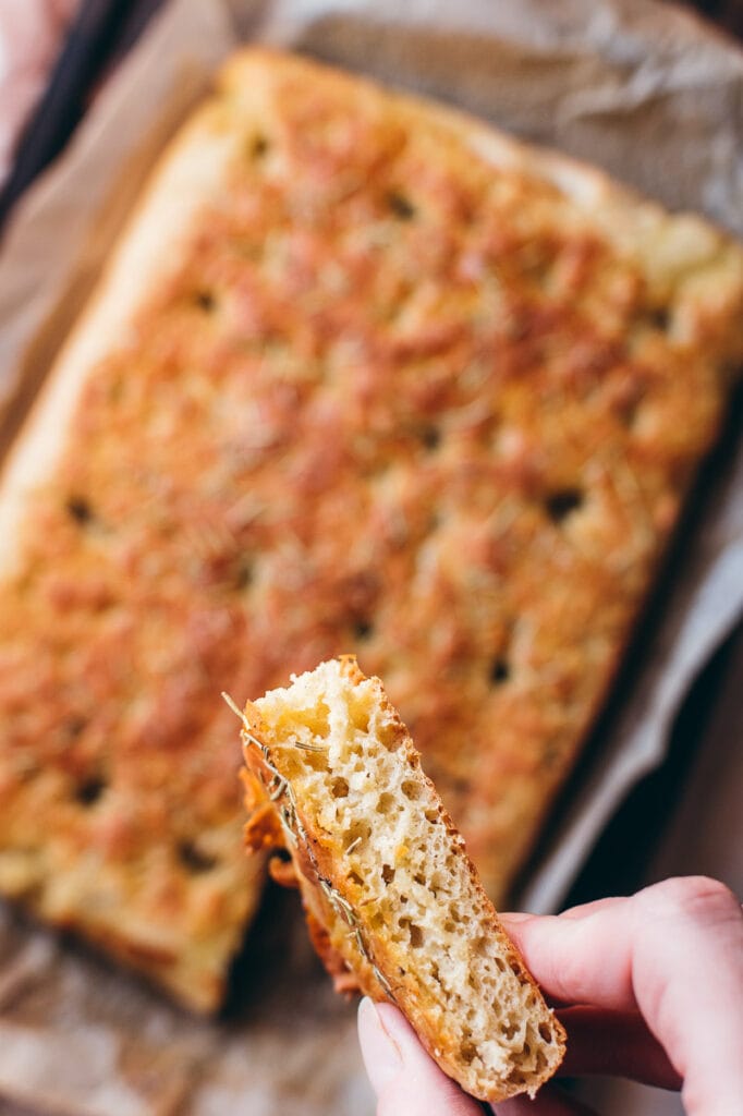 a hand holding a slice of gluten free vegan focaccia bread displaying the interior texture