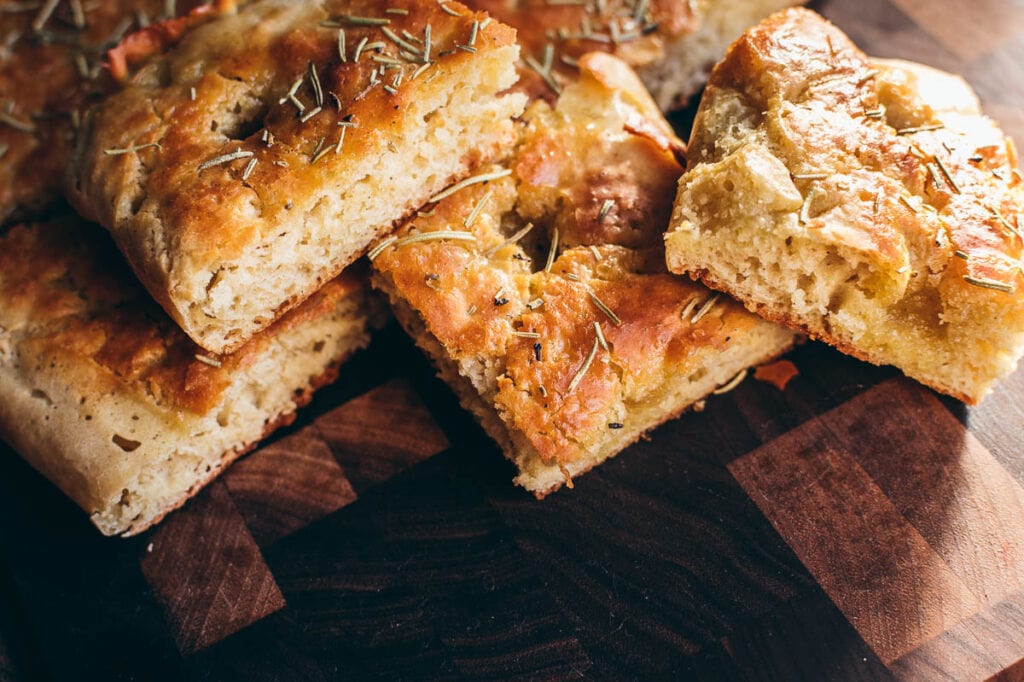 square slices of gluten free focaccia resting on a dark wood cutting board