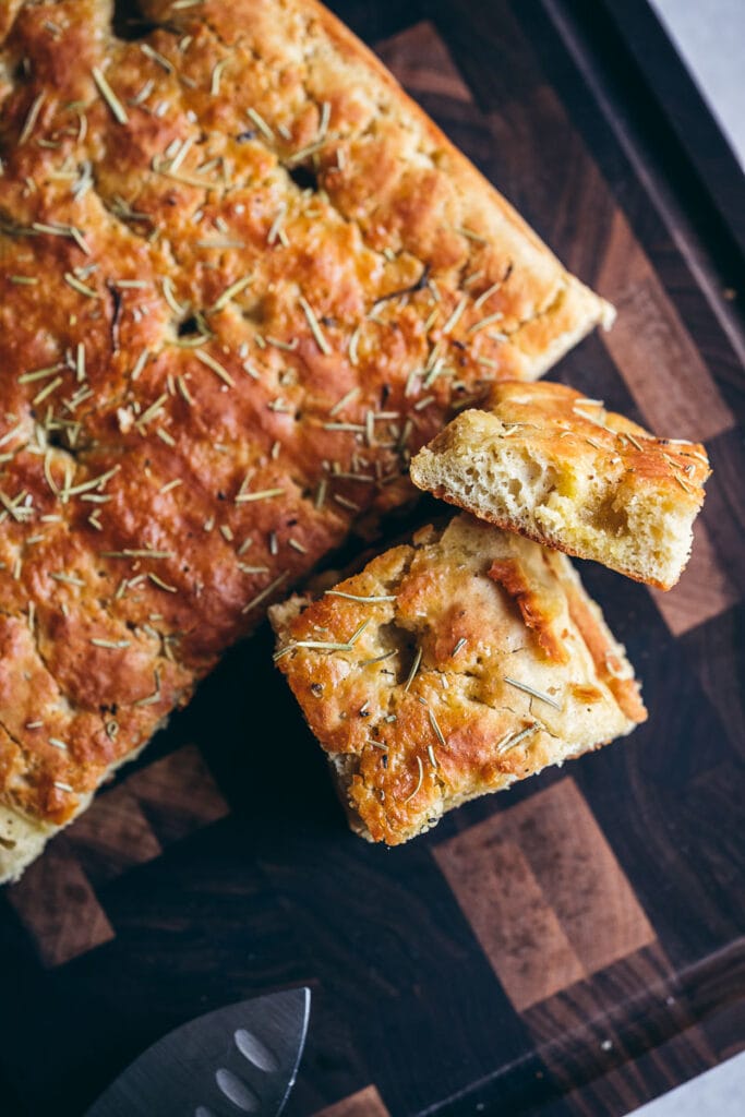 a loaf of freshly baked gluten free vegan focaccia bread resting on a dark wooden cutting board