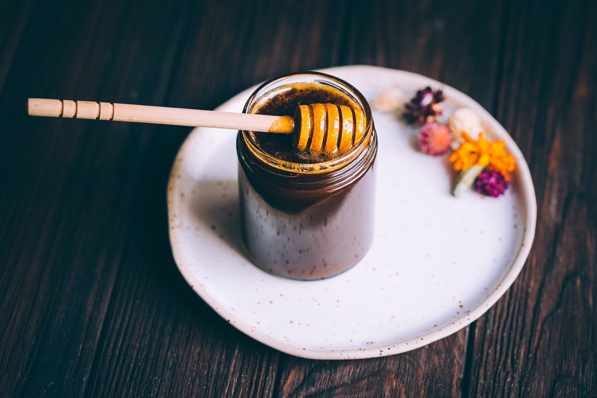 A jar of dark vegan honey resting on a white ceramic plate.