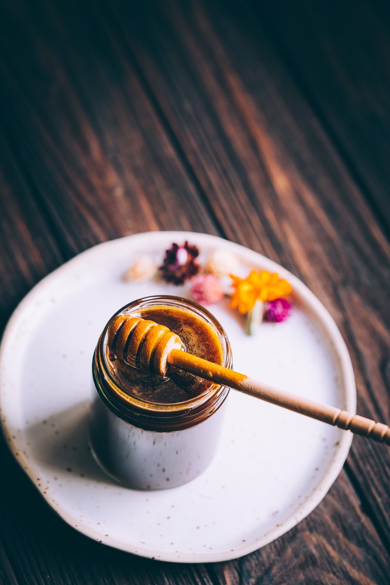 Dried flowers resting on a white plate next to an open jar of honey substitute.