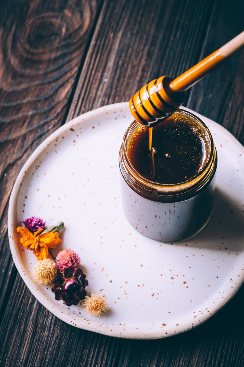 A honey dipper dipping into a clear jar of dark honey.