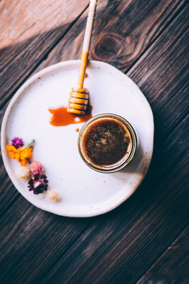 An open jar of honey resting on a ceramic plate drizzled with a honey dipper.