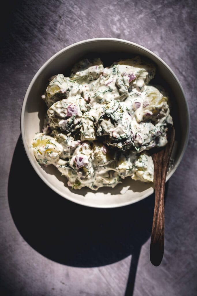  a hardlight image of a white ceramic bowl filled with creamy vegan potato salad lit by the sun